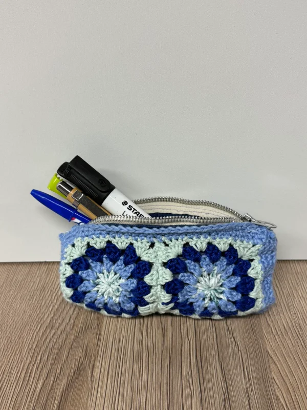 Pochette crochetée bleue et verte avec des fleurs, contenant des stylos et un marqueur.
