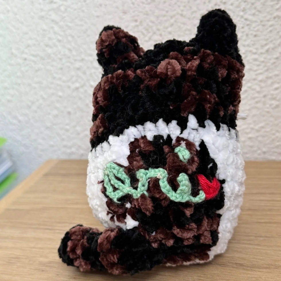 Petit ours en peluche brun, noir et blanc avec des yeux verts et une bouche rouge