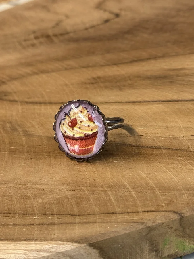 Bague fantaisie cabochon cupcake 1 Un petit cupcake glacé illustre ce cabochon, dans le même esprit gourmand que nos bagues tartes. Monture argentée ajustable. Fait main à Arras, pièce unique. Entretien : évitez le contact prolongé avec l'eau et les cosmétiques. Tags : bague fantaisie, bague fait main, cabochon cupcake, bague gourmande, bague ajustable, bague pièce unique