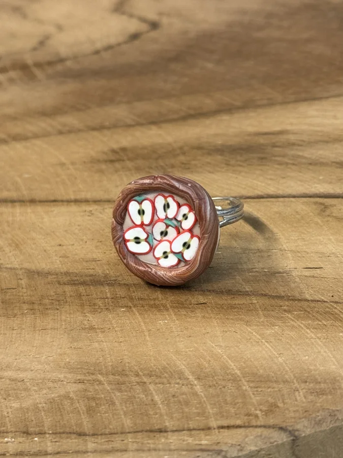 Dernière gourmandise de la série : cette bague reproduit une tarte aux pommes miniature, avec de fines lamelles disposées en éventail sur le dôme, comme une vraie tarte tout juste sortie du four. La bordure façon pâte torsadée, ici en finition argentée, complète l'illusion. Caractéristiques : Dôme façon tarte aux pommes, lamelles modelées à la main Bordure façon pâte torsadée, monture argentée Fait main à Arras Pièce unique Entretien : évitez les frottements répétés et l'exposition prolongée au soleil. Envie d'une autre gourmandise ? Toute la collection est ici.